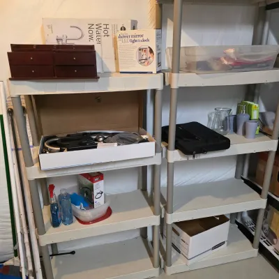 Sale Photo Thumbnail #48: Two multi-tier plastic shelving units holding various household goods, boxed items, bathroom accessories, and storage containers.