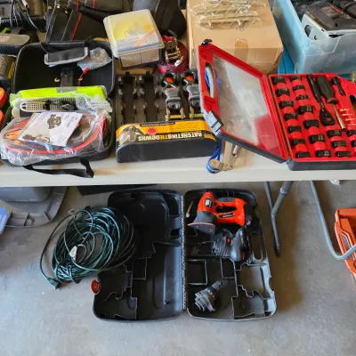 Sale Photo Thumbnail #127: Assortment of hand tools, hardware, and automotive supplies, including a socket set, ratcheting tie-downs, jumper cables, and an electric power tool in a hard case.