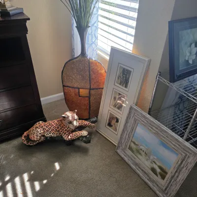 Sale Photo Thumbnail #87: Collection of home decor including a spotted leopard figurine lounging on a branch, a tall textured ceramic floor vase, and framed artwork resting on the floor.