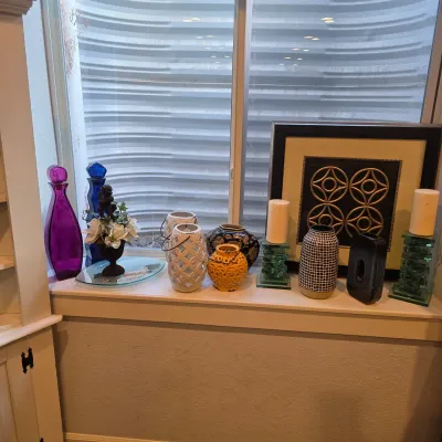 Sale Photo Thumbnail #34: Collection of decorative home accents displayed on a windowsill, including colorful glass bottles, ceramic vases, lattice lanterns, stacked glass candle holders, and framed artwork.