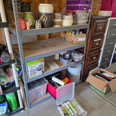 Sale Photo Thumbnail #136: Heavy-duty metal shelving unit loaded with ceramic pots, painting supplies, a boxed Workpro electric paint sprayer, and various storage bins.