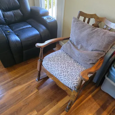 Sale Photo Thumbnail #103: Vintage wooden rocking chair featuring an upholstered grey-and-white patterned seat cushion and a throw pillow, shown alongside a black leather power recliner.