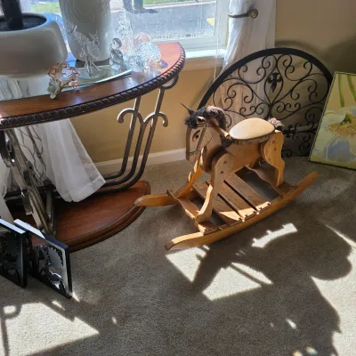 Sale Photo Thumbnail #98: Vintage handcrafted wooden rocking horse with upholstered seat and mane detailing, displayed next to a wrought iron half-moon console table.
