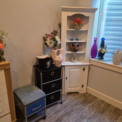 Sale Photo Thumbnail #33: White painted cottage-style corner hutch paired with a contemporary three-drawer rolling storage cart and a blue upholstered ottoman.