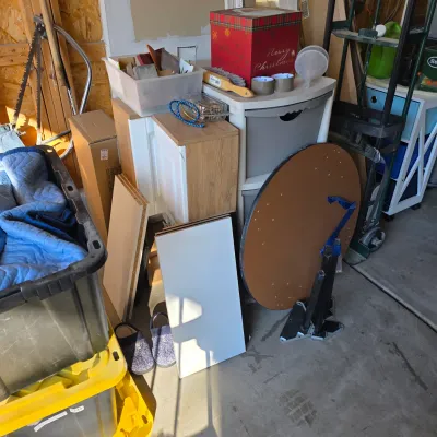 Sale Photo Thumbnail #133: Assorted workshop items, home organization units, moving blankets in a plastic tote, and a circular wooden tabletop in a garage setup.