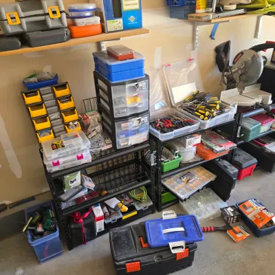Sale Photo Thumbnail #124: Workshop storage setup featuring metal shelving units filled with plastic toolboxes, small parts organizers, screwdrivers, pliers, and a miter saw on the side.