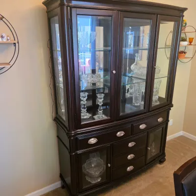 Sale Photo Thumbnail #71: Traditional dark wood china hutch with glass display doors, interior lighting, and lower storage drawers, filled with cut crystal items.