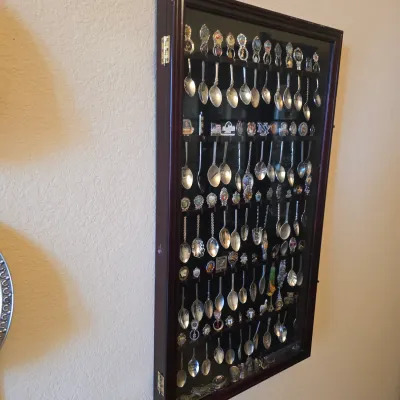 Sale Photo Thumbnail #70: Wall-mounted glass-front shadow box display case filled with a collection of vintage souvenir spoons.