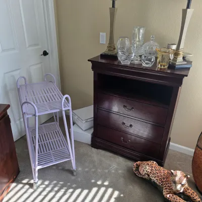 Sale Photo Thumbnail #86: Dark wood three-drawer media chest displaying crystal glassware alongside a light purple painted metal rolling utility cart.