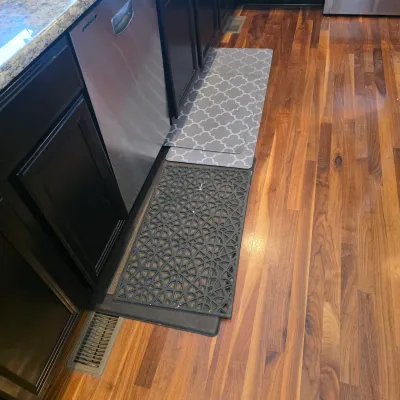 Sale Photo Thumbnail #117: Selection of kitchen floor mats, including patterned anti-fatigue mats and a black geometric rubber runner, placed on hardwood flooring.