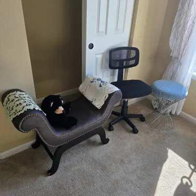 Sale Photo Thumbnail #100: Selection of seating featuring a faux-leather scroll-arm chaise bench with nailhead trim, a black mesh rolling desk chair, and a wire-frame vanity stool.