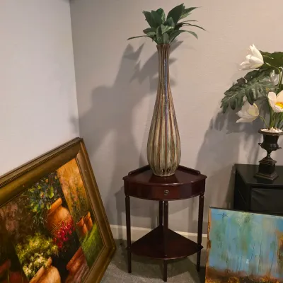 Sale Photo Thumbnail #19: Tall glazed ceramic floor vase displaying faux greenery, resting on a dark wood corner table alongside framed artwork.