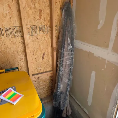 Sale Photo Thumbnail #159: Tall outdoor patio umbrella wrapped in plastic protective sheeting, stored in a corner.