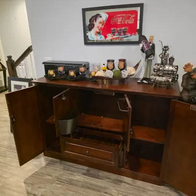 Sale Photo Thumbnail #7: Traditional dark wood sideboard bar cabinet with fold-out doors, built-in ice bucket, and wine storage drawer, displayed alongside barware decor and a framed Coca-Cola mirror.