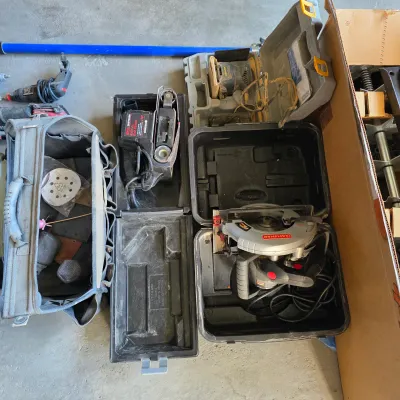 Sale Photo Thumbnail #142: Collection of power tools including a Craftsman circular saw, belt sander, finishing sander, and a canvas tool bag filled with sanding pads.