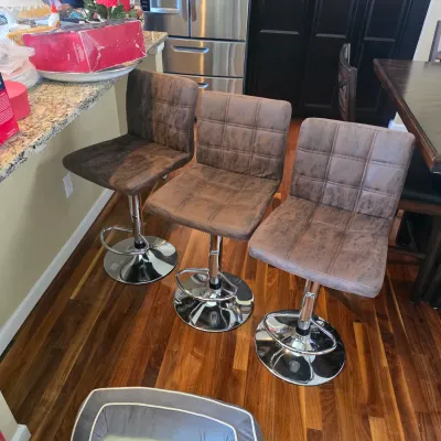 Sale Photo Thumbnail #102: Set of three modern barstools featuring distressed brown faux-leather tufted seats, chrome pedestal bases, integrated footrests, and height-adjustable swivels.