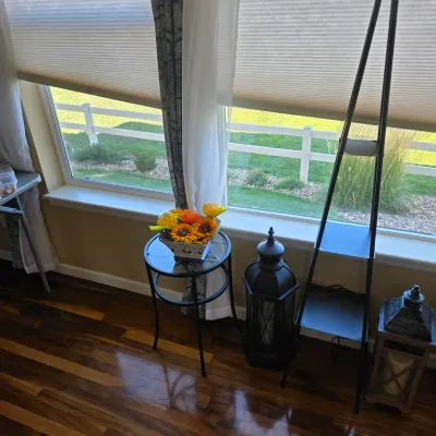Sale Photo Thumbnail #107: Collection of home decor including a round metal glass-top side table with artificial sunflowers, decorative lanterns, and a modern black ladder shelf.