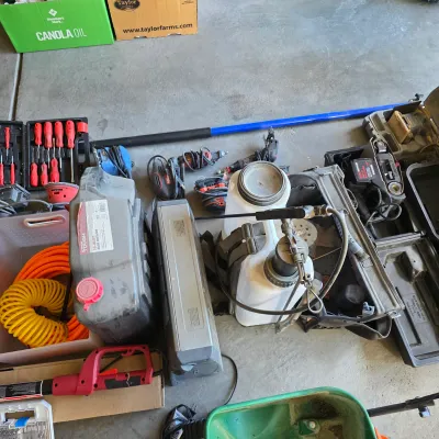 Sale Photo Thumbnail #141: Collection of lawn care equipment and power tools, including a backpack sprayer, fluid drain containers, coiled hoses, and various hand sanders.