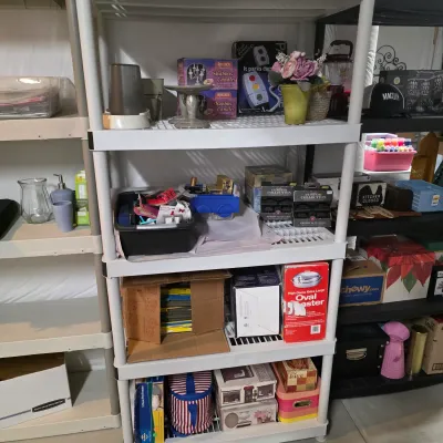 Sale Photo Thumbnail #49: White four-tier plastic shelving unit holding an assortment of household items, boxed goods, candles, and decorative pieces.
