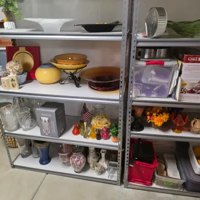 Sale Photo Thumbnail #53: Metal shelving units filled with various glassware, ceramic bowls, a boxed Waterford crystal vase, small decorative items, and craft supplies.
