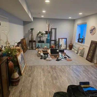Sale Photo Thumbnail #4: Spacious finished basement room filled with home decor, framed wall art, decorative vases, side tables, electronics, and small home goods organized for an estate sale.