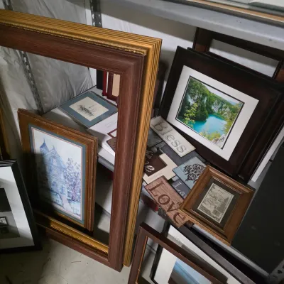 Sale Photo Thumbnail #61: Collection of assorted picture frames, framed artwork, and decorative wall signs stored on shelving.