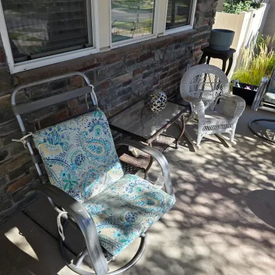 Sale Photo Thumbnail #118: Patio furniture set including a metal motion armchair with teal paisley cushions, a glass-top wicker side table, and a white wicker child's rocking chair.