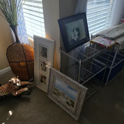Sale Photo Thumbnail #88: Collection of home decor items featuring a ceramic leopard figurine, tall floor vase with faux greenery, framed wall art, and wire shelving units.