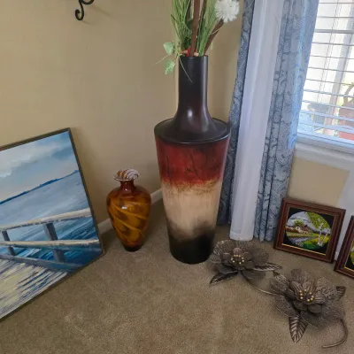 Sale Photo Thumbnail #81: Collection of home decor including a tall ombre floor vase with artificial greenery, an amber swirl glass vase, framed wall art, and metal floral sculptures.