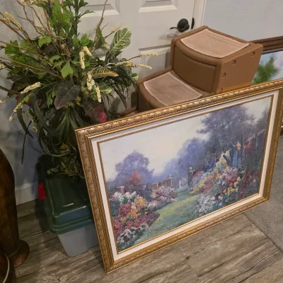 Sale Photo Thumbnail #15: Large framed impressionist-style garden scene art print in an ornate gold-tone frame, resting on the floor beside artificial house plants.
