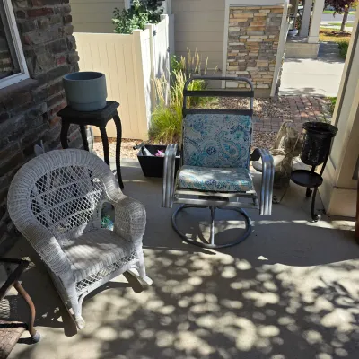 Sale Photo Thumbnail #119: Collection of patio furniture featuring a white wicker rocking chair and a metal swivel patio chair with a patterned cushion.