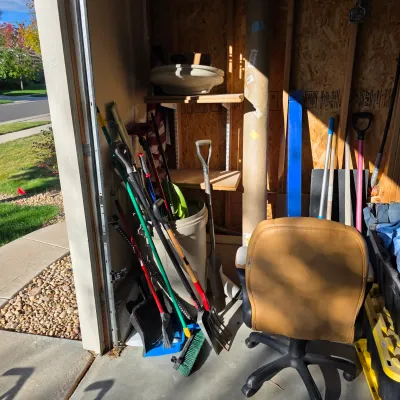 Sale Photo Thumbnail #132: Collection of various lawn and garden hand tools, shovels, brooms, and a tan vinyl office chair inside a storage shed.