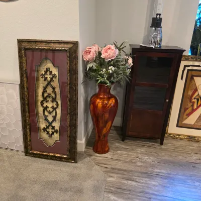 Sale Photo Thumbnail #24: A tall, mottled orange ceramic floor vase filled with faux pink peonies, alongside a dark wood display cabinet and framed traditional wall art.