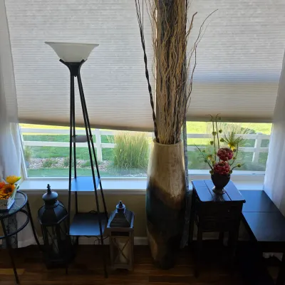 Sale Photo Thumbnail #106: A collection of contemporary home decor including a metal tripod floor lamp with tiered shelves, a tall ceramic floor vase with decorative dried branches, and decorative lanterns.