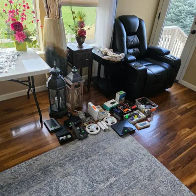 Sale Photo Thumbnail #160: Living room setup featuring a black leather power recliner, accent lanterns, and an assortment of video game consoles and electronics displayed on the floor.