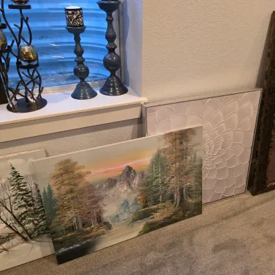 Sale Photo Thumbnail #23: Selection of framed and unframed wall art, featuring landscape paintings and a textured floral canvas, alongside decorative dark blue candlesticks on a windowsill.