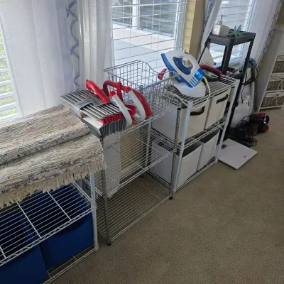 Sale Photo Thumbnail #90: Wire shelving units containing folded rag rugs, red handle grippers, fabric storage bins, and a modern clothes iron.