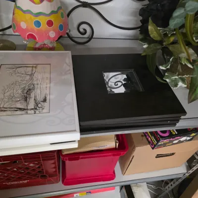Sale Photo Thumbnail #59: A shelf displaying framed landscape artwork, a black photo frame, colorful table decor, and plastic storage crates beneath.