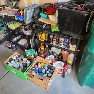 Sale Photo Thumbnail #145: Assorted garage and automotive supplies, including two boxes filled with spray paint cans, cleaning chemicals, and tools on shelving units.