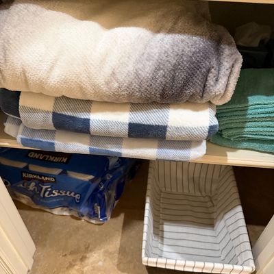 Sale Photo Thumbnail #150: Linen closet featuring folded plush blankets, bath towels, a Kirkland bath tissue pack, and a striped fabric storage basket.