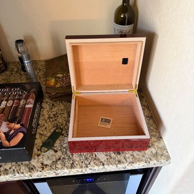 Sale Photo Thumbnail #51: Polished wooden desktop humidor shown open alongside a cigar cutter and a box of Pride of Copan cigars.