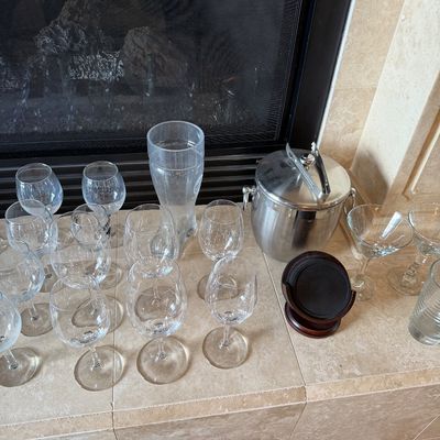 Sale Photo Thumbnail #38: Assorted barware collection featuring various stemware glasses, a boot-shaped glass, martini glasses, and a stainless steel ice bucket with tongs.