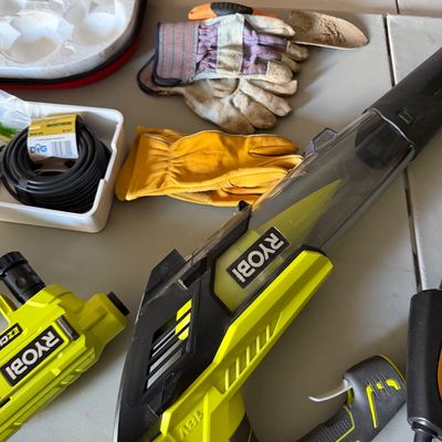 Sale Photo Thumbnail #71: Ryobi 18V ONE+ hand vacuum, pressure washer tool, work gloves, and irrigation tubing displayed on a table.