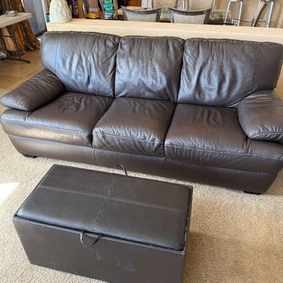 Sale Photo Thumbnail #225: Contemporary dark brown leather three-cushion sofa featuring pillow-top arms and visible stitching, paired with a matching rectangular storage ottoman.