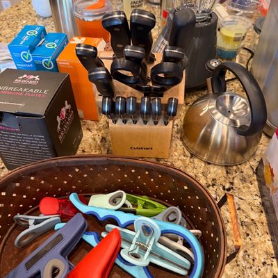 Sale Photo Thumbnail #170: Collection of kitchen items including a basket filled with various colorful bag clips, a Cuisinart knife block set, a stainless steel tea kettle, and a blender.