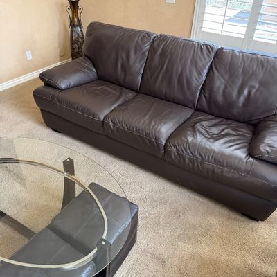 Sale Photo Thumbnail #228: Contemporary dark brown leather three-cushion sofa featuring white contrast stitching, paired with an oval glass-top coffee table and matching leather ottomans.
