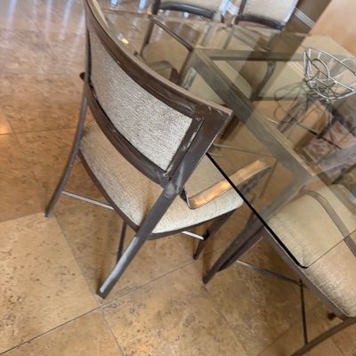 Sale Photo Thumbnail #205: Modern glass-top dining table with a dark metallic frame, paired with matching chairs featuring upholstered seats and back panels.