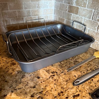 Sale Photo Thumbnail #172: Non-stick rectangular roasting pan with a removable wire rack and side handles, displayed alongside kitchen utensils.