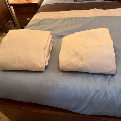 Sale Photo Thumbnail #138: Two folded white bed sheets displayed on a blue and brown striped bedspread.