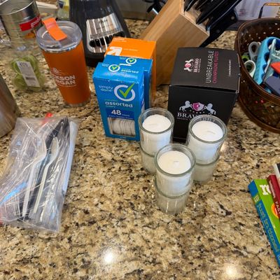 Sale Photo Thumbnail #164: Collection of kitchen items including an Osterizer blender, a knife block, small glass votive candles, disposable cutlery, and an orange insulated tumbler.
